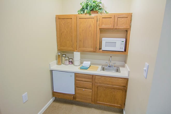 A small kitchenette with wooden cabinets, a microwave, and a sink.