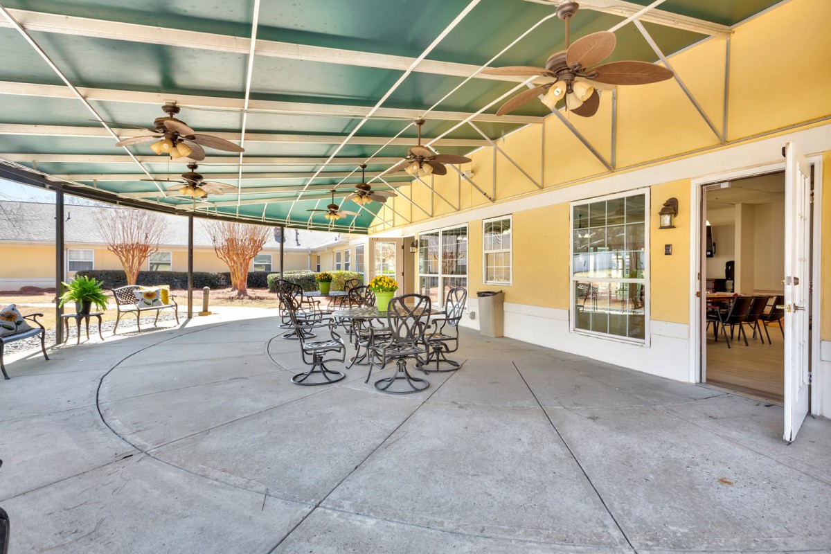 A covered outdoor patio with ceiling fans, metal chairs, and a yellow building backdrop.