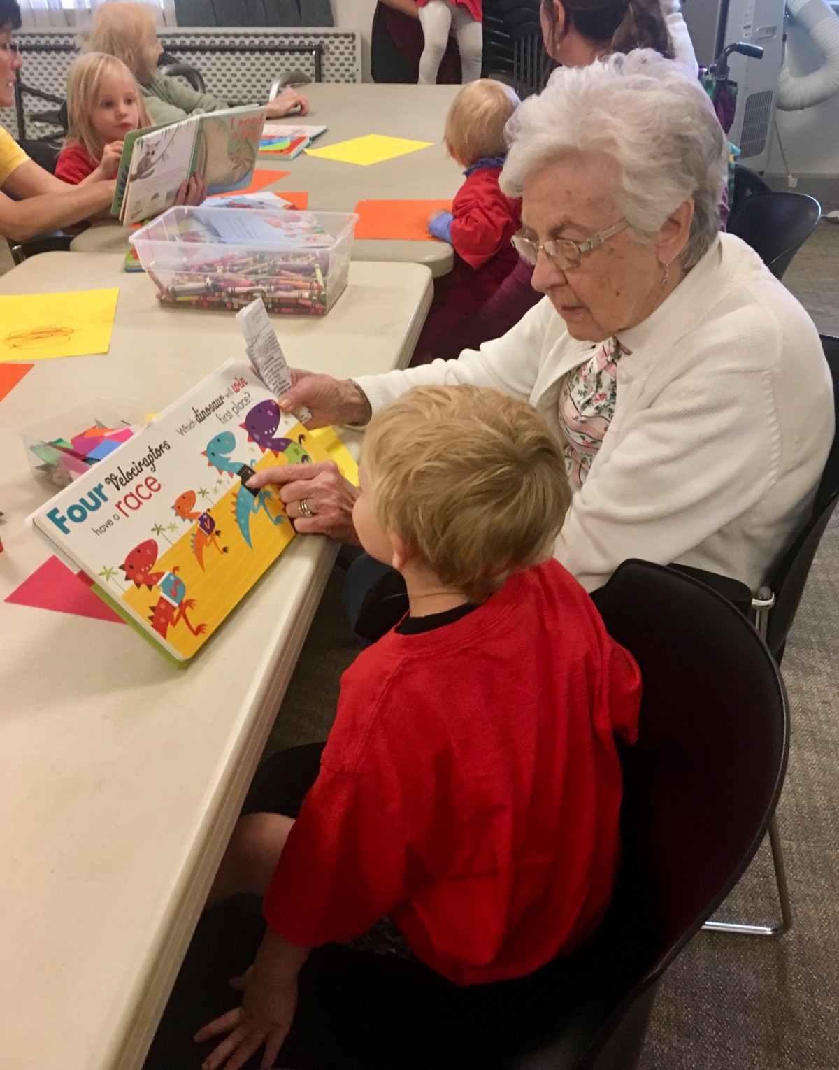An adult reading a book to a child at a table.