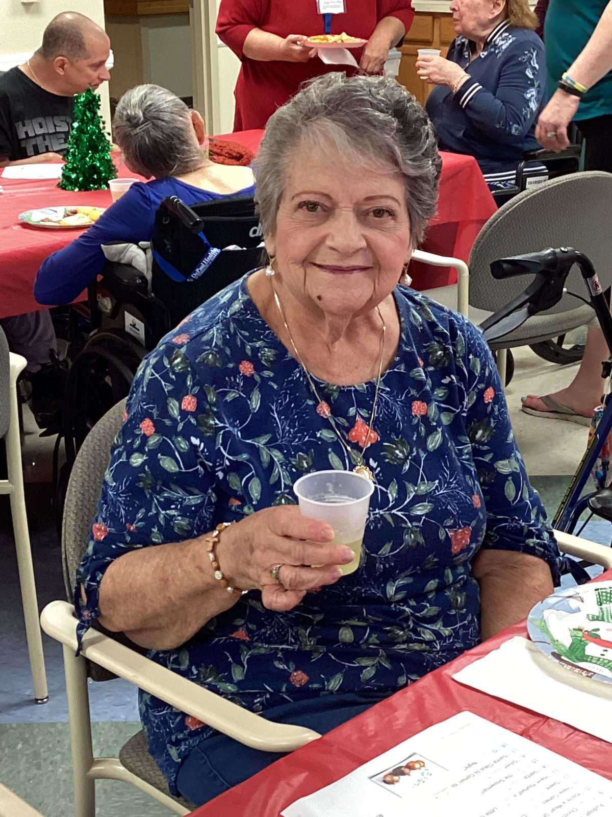 An elderly woman smiling and holding a cup at a social gathering.