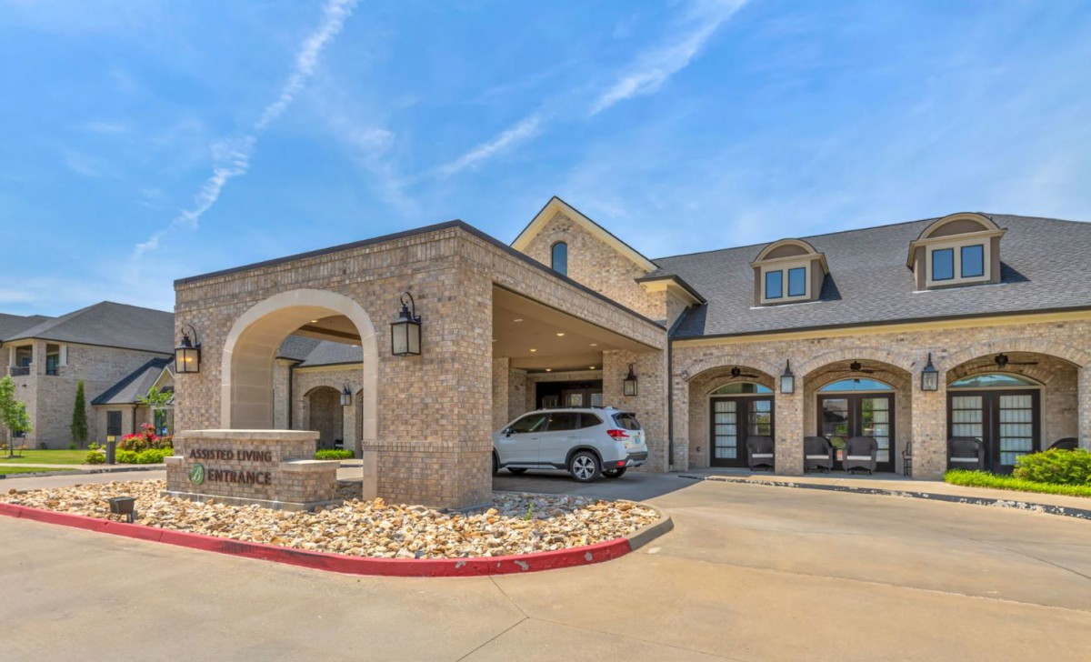 A modern brick building entrance with an arched driveway and a parked car.