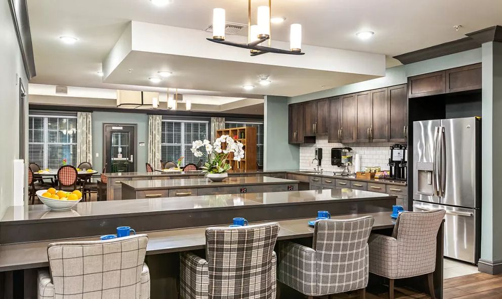 A modern kitchen with a large central island, surrounded by plaid upholstered chairs and featuring sleek dark cabinetry.
