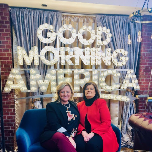 Two women posing together in front of a 'Good Morning America' backdrop.