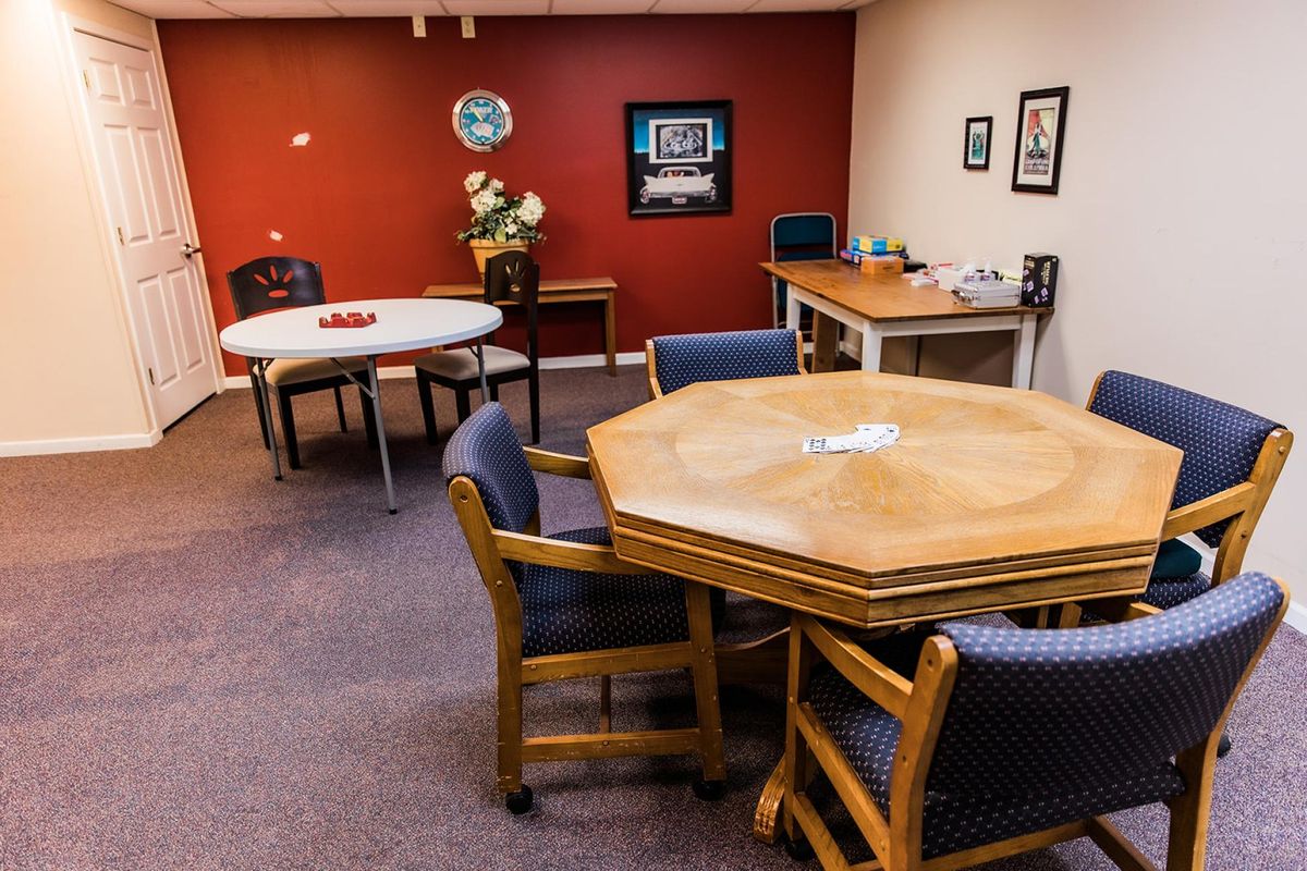 A cozy office meeting room with a red accent wall, featuring multiple tables and chairs for discussions.