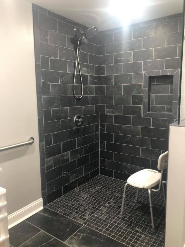 A modern walk-in shower with black tiles and a built-in seat.