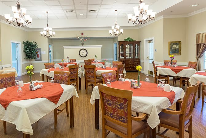 A well-decorated dining area with arranged tables and chairs, featuring chandeliers and a wooden floor.