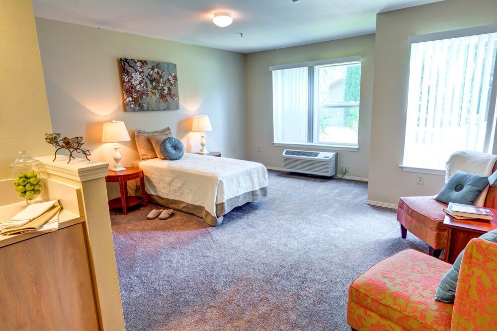 A cozy bedroom with a single bed, bedside tables with lamps, and large windows.