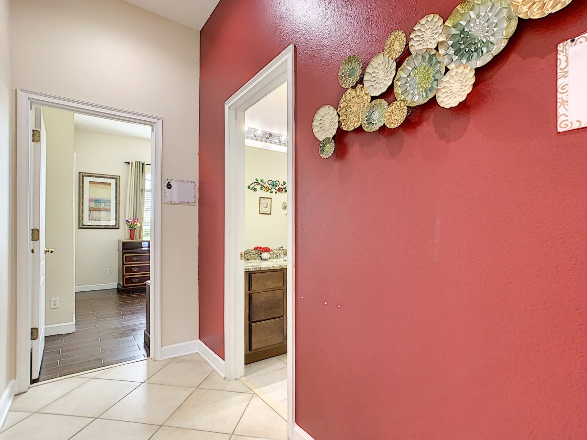 A hallway with a bold red accent wall adorned with decorative plates, featuring doorways leading to other rooms and tiled flooring.