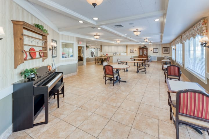 A spacious room with a piano, tables, and chairs arranged on tiled flooring.