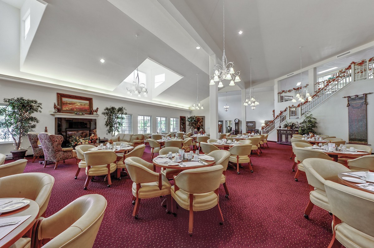 A spacious restaurant dining area with elegant chandeliers, comfortable seating, and a red carpeted floor.