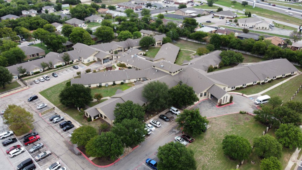 Aerial view of a suburban residential complex with surrounding trees and a parking area.