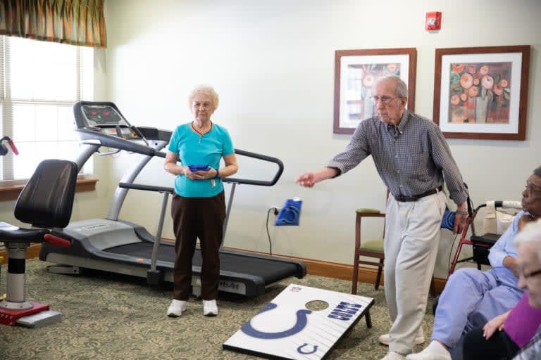 Two seniors enjoying a game of cornhole in an exercise room.