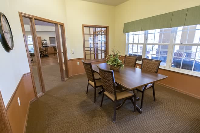 A cozy dining area with a wooden table and four chairs, featuring large windows and decorated with a plant centerpiece.