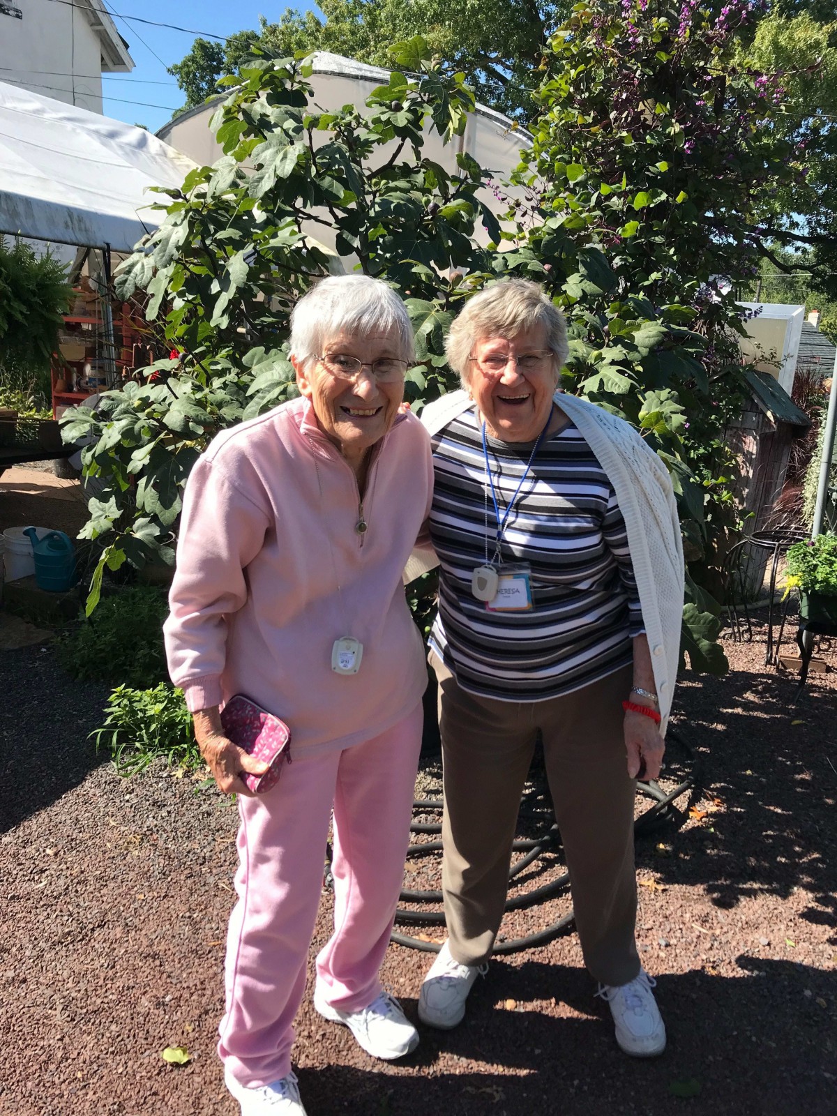 Two elderly individuals smiling together outdoors in a garden setting.