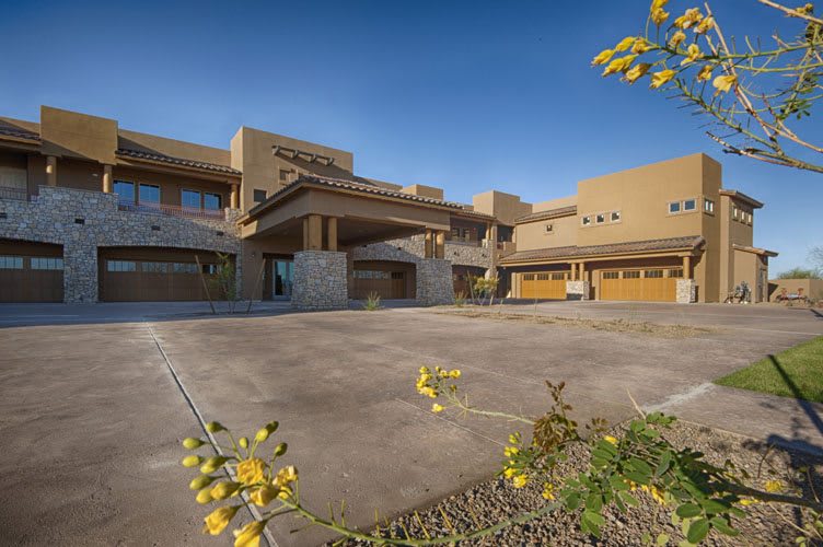 A modern building with a spacious driveway and landscaped surroundings on a sunny day.