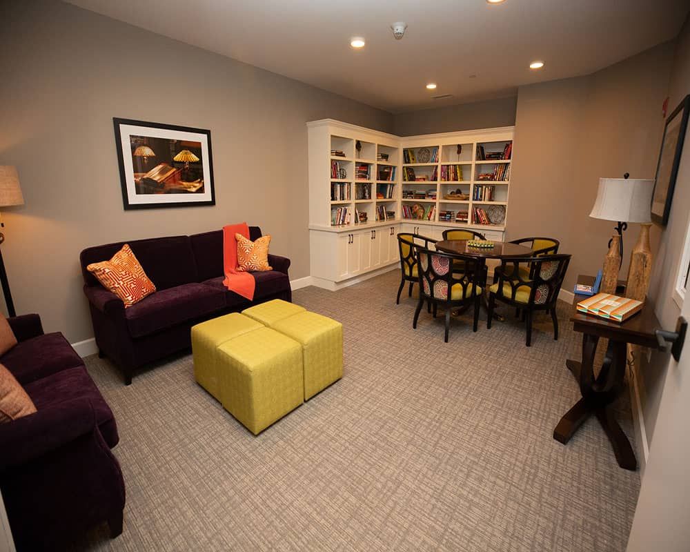 A cozy living room with a sofa, ottoman, bookshelves, and a dining table set.