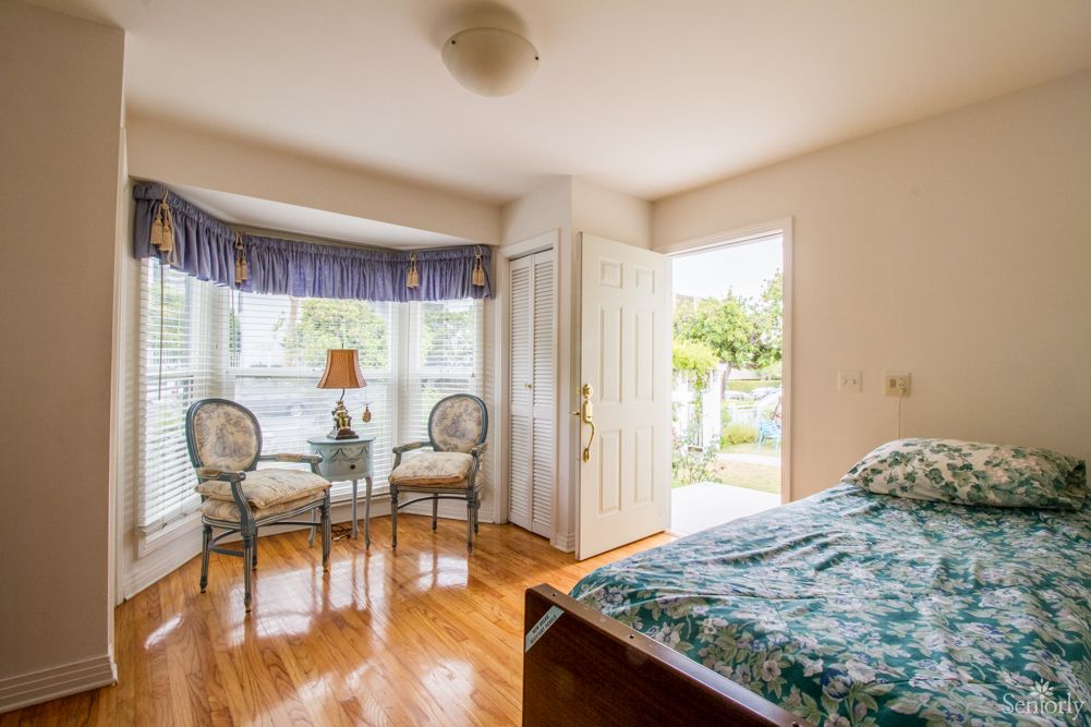 A bright bedroom with a bay window, showcasing a cozy seating area and access to an outdoor space.