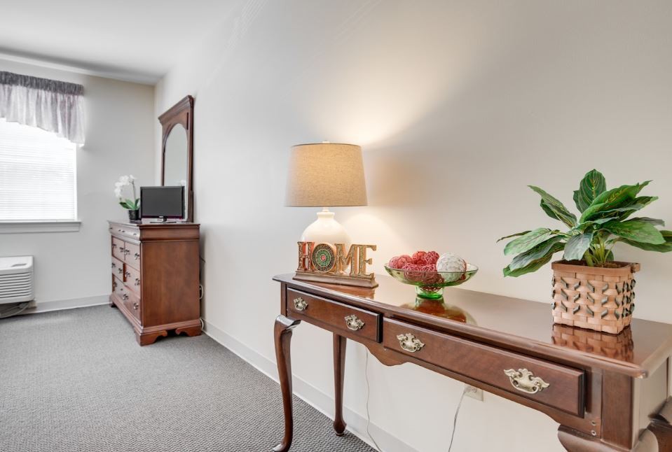 A warmly lit room featuring a wooden console table adorned with a lamp, decorative items, and a mirror in the background.