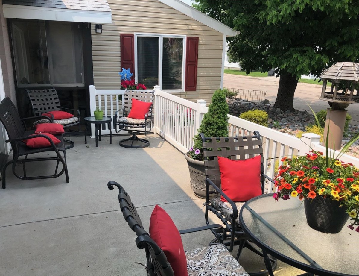 Cozy patio setting with red-cushioned chairs and potted plants outside a house.