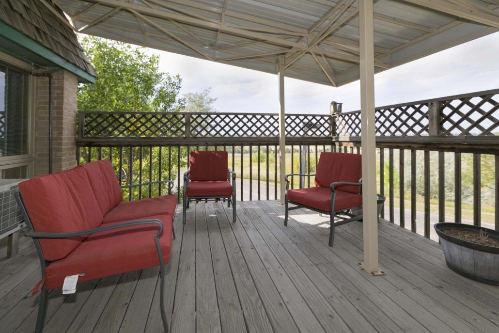 A cozy outdoor patio with red cushioned chairs under a canopy, set on a wooden deck with lattice fencing.