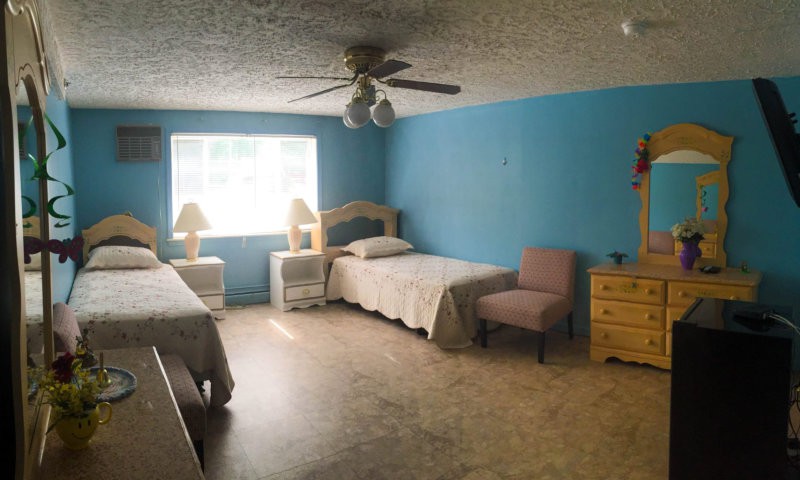 A bedroom with two beds, a ceiling fan, and various furniture pieces.