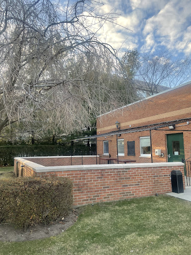A view of a brick building surrounded by grass and trees under a cloudy sky.