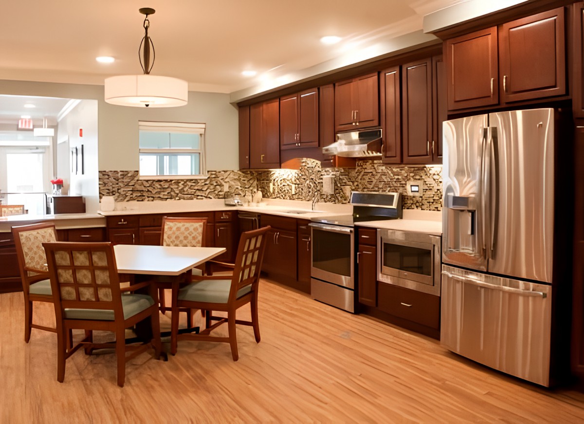 A modern kitchen with wood cabinets, stainless steel appliances, and a small dining area.