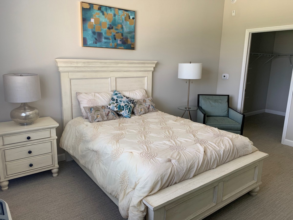 A cozy bedroom with a neatly made bed, modern lamp, armchair, and artistic wall decor.