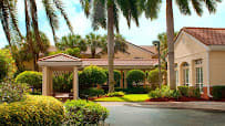A tropical building entrance surrounded by palm trees and lush greenery.