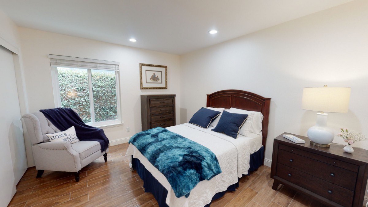 A cozy bedroom with a neatly made bed featuring blue and white bedding, a nightstand, and a chest of drawers.