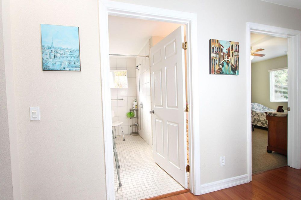A view through a doorway into a bright, clean bathroom, with paintings adorning the walls.