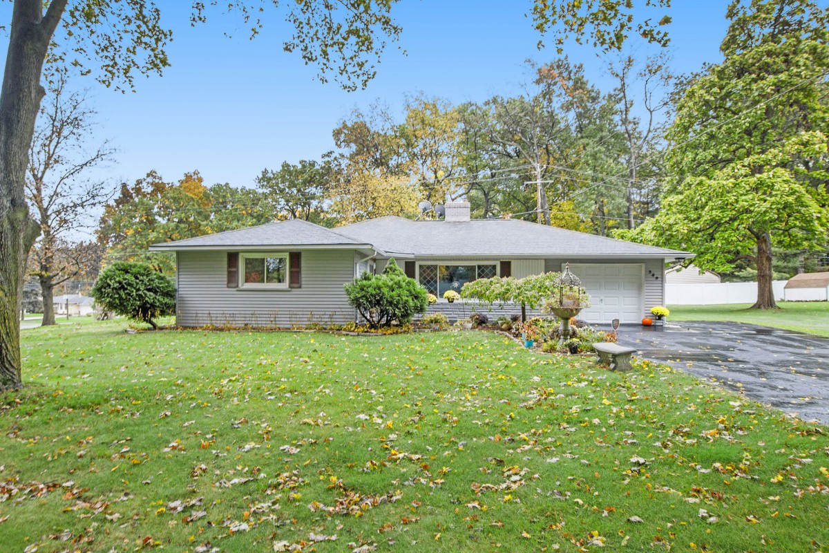 A ranch-style house with a spacious front yard and surrounding trees in a suburban neighborhood.