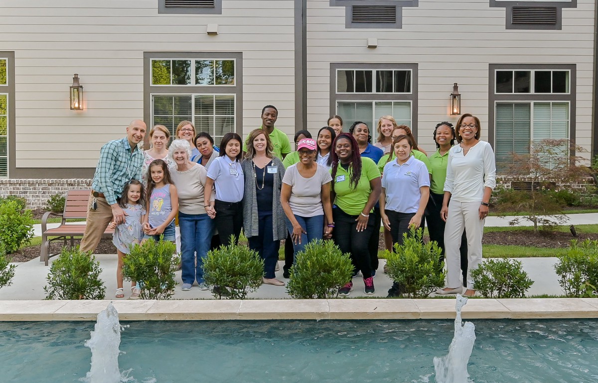 A diverse group of people posing together in front of a house with a pool and garden.