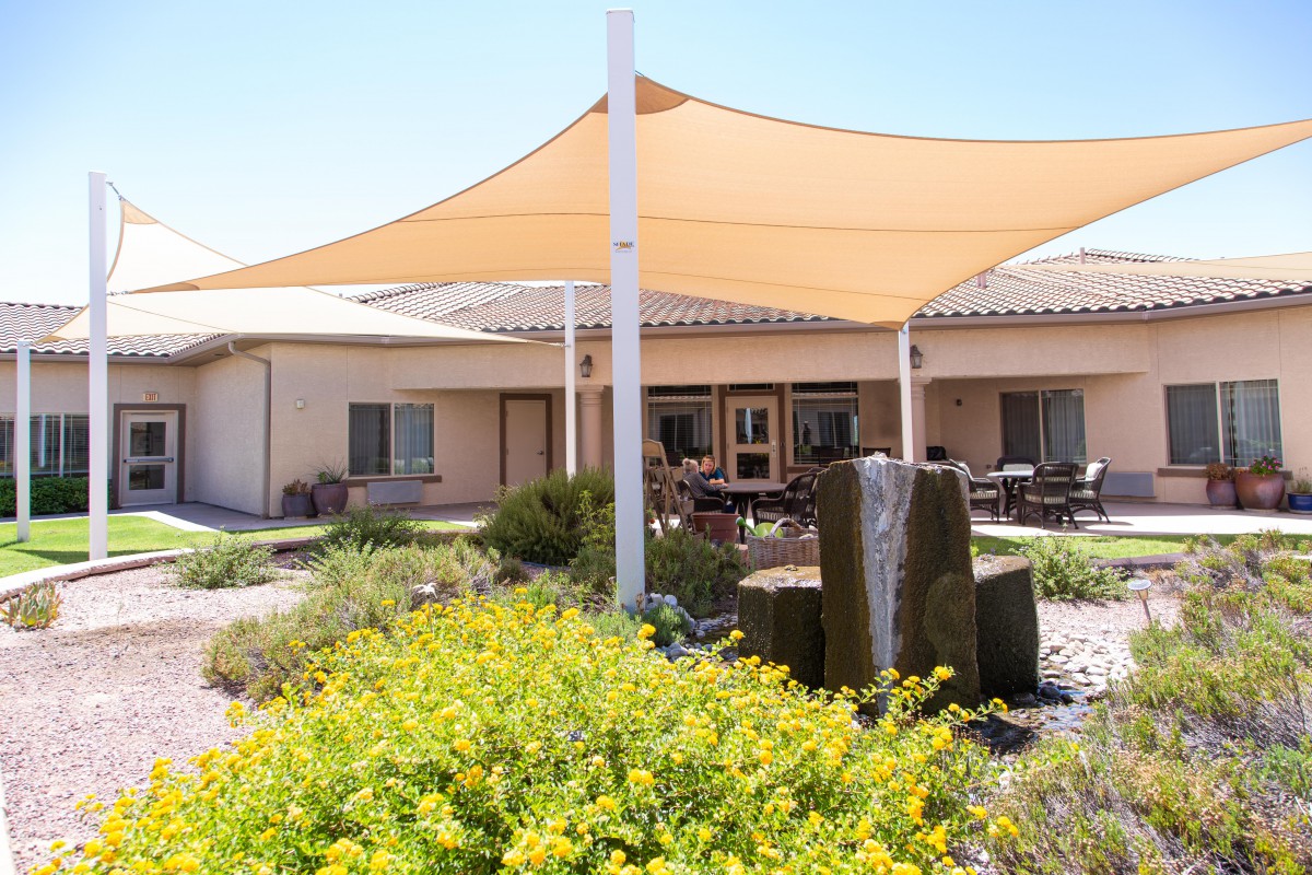 A peaceful outdoor patio area featuring a shade sail, fountain, and lush landscaping.