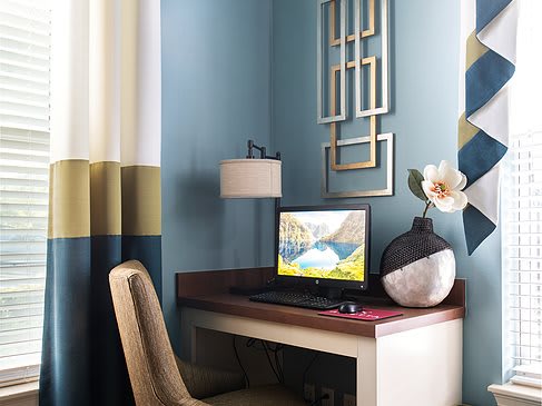 A stylish home office setup with a modern desk and computer, complemented by a decorative lamp and vase against blue walls.