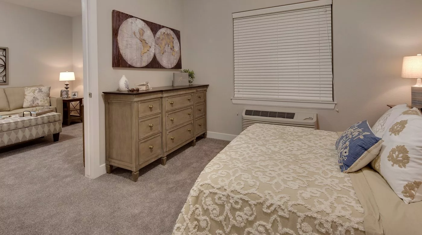 A cozy bedroom featuring a wooden dresser, elegant artwork, and a neatly made bed.