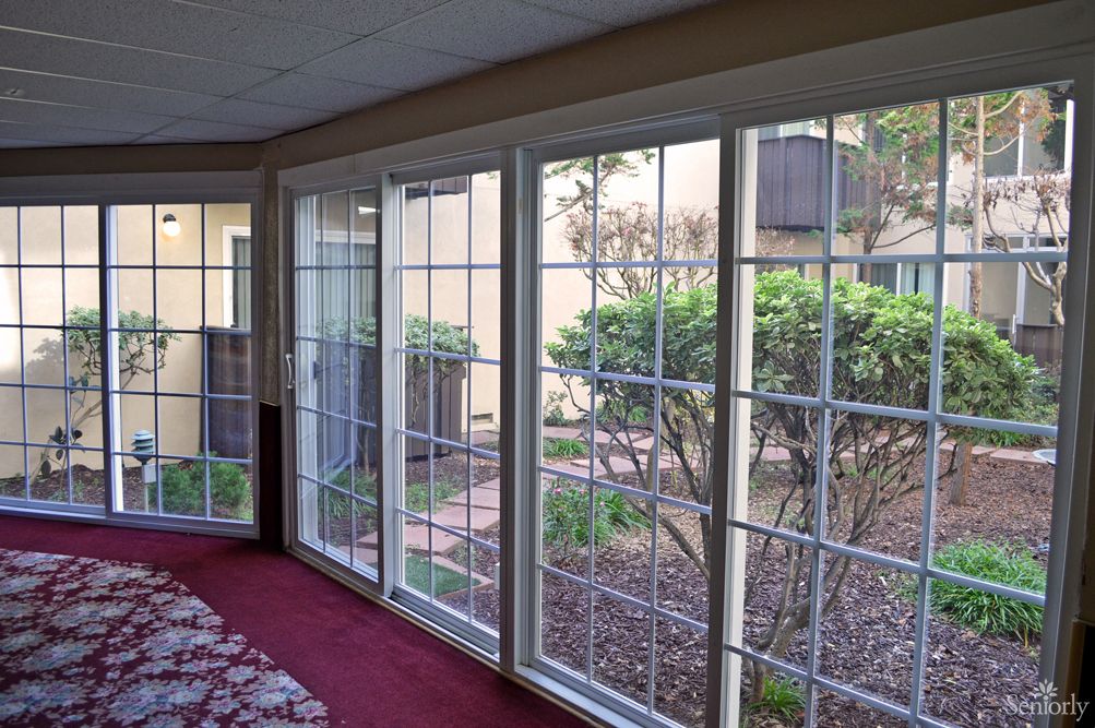 A bright sunroom with large glass windows offering a view of a garden.