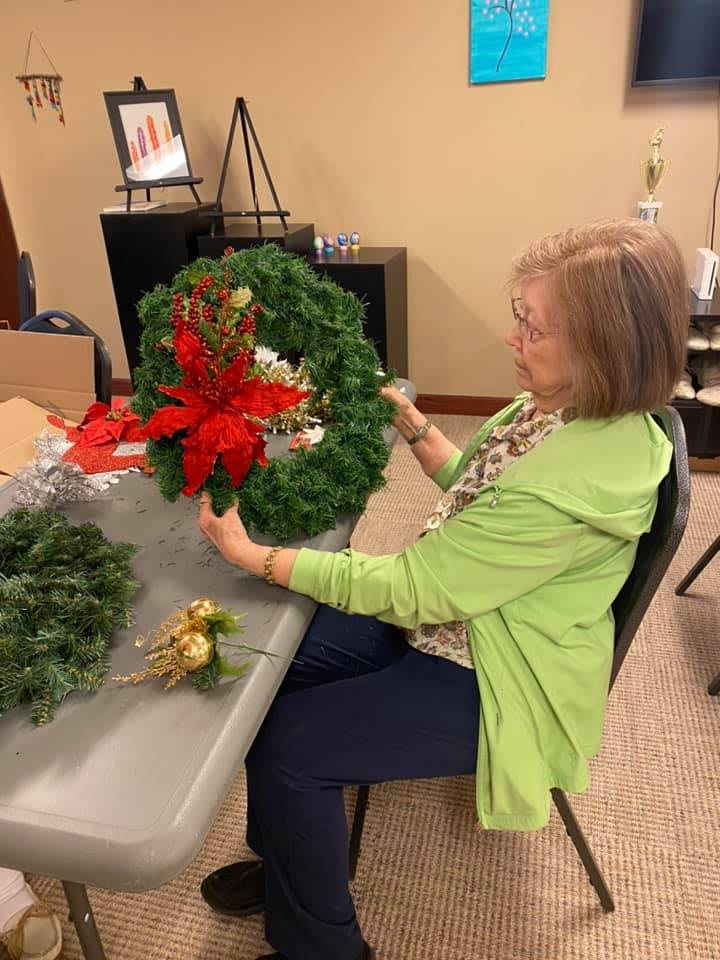 A woman decorates a wreath with festive elements at a table indoors.