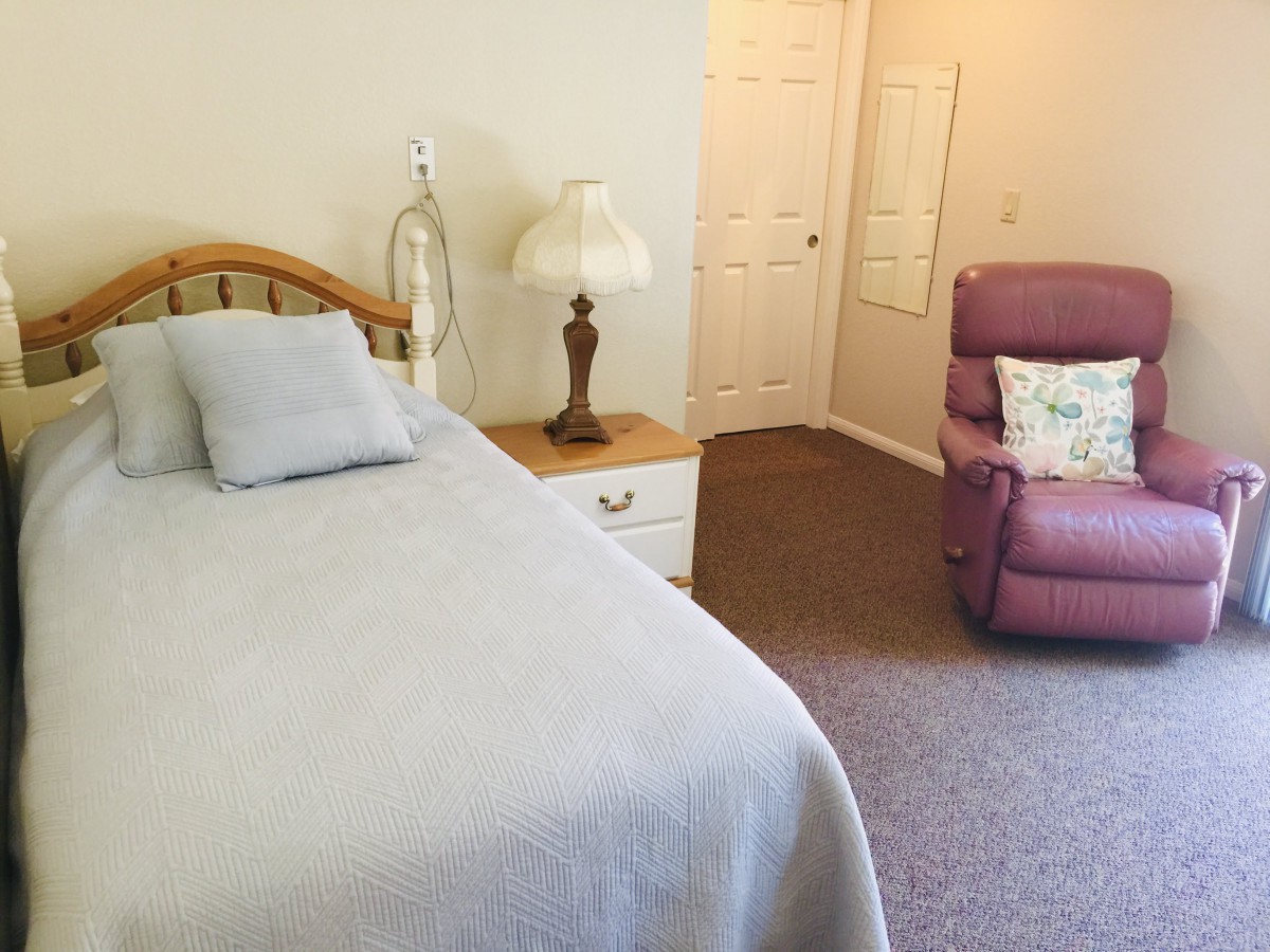 A cozy bedroom featuring a bed, nightstand with a lamp, and a cushy recliner chair.