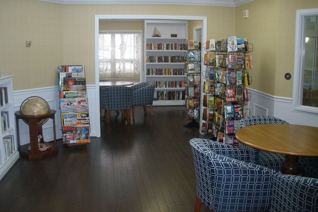 A cozy library reading area with bookshelves, tables, and chairs.