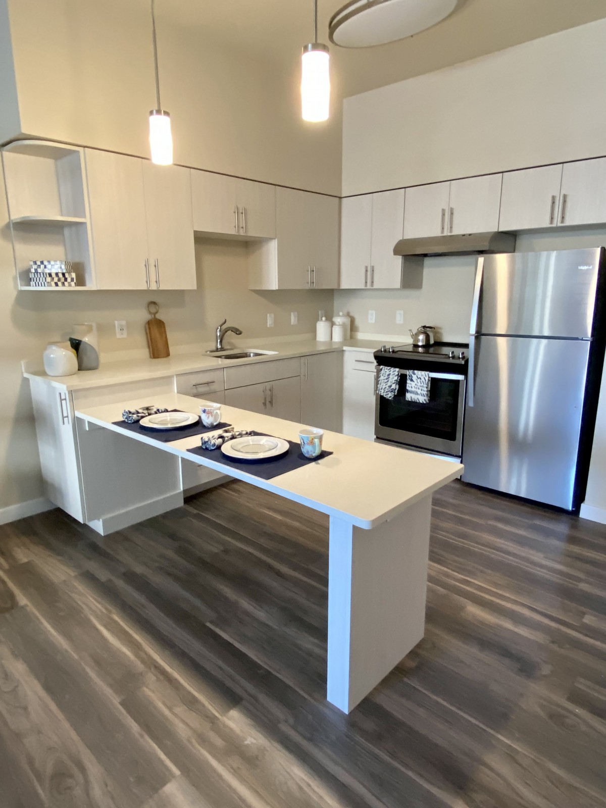 A modern kitchen with stainless steel appliances, featuring an open dining area and wood flooring.