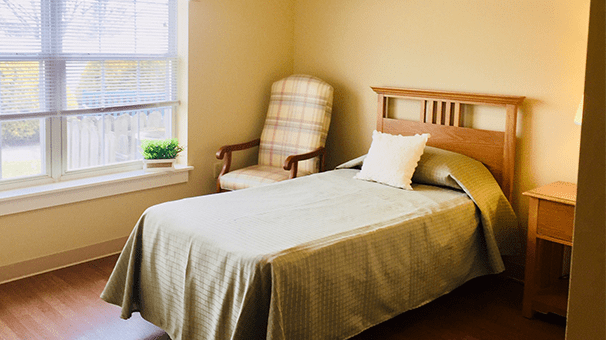 A minimalist bedroom with a single bed, armchair, and a window letting in natural light.