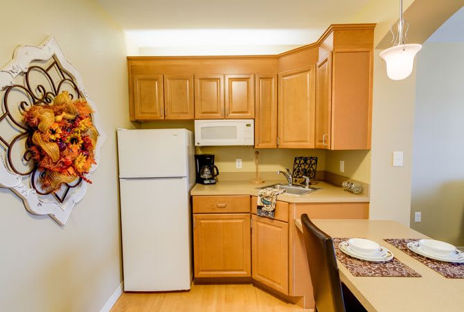 A cozy kitchen with wooden cabinets, featuring a refrigerator and microwave.