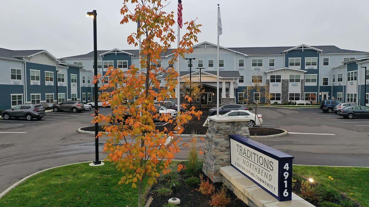 A modern building with autumn foliage, flags, and a sign in the foreground.