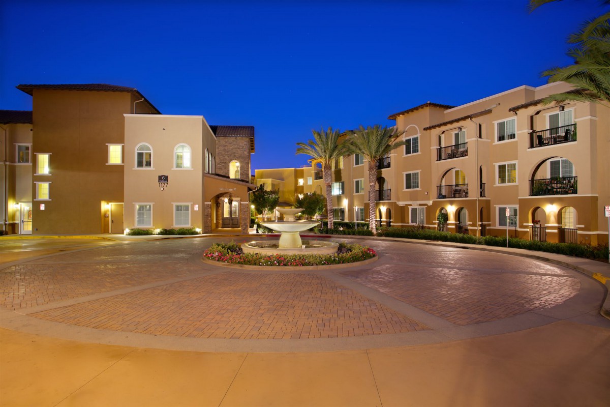 A beautifully lit apartment courtyard with a central fountain at night.