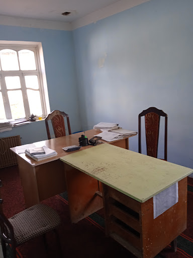 A simple office setup featuring a desk and chairs, illuminated by natural light from the window.