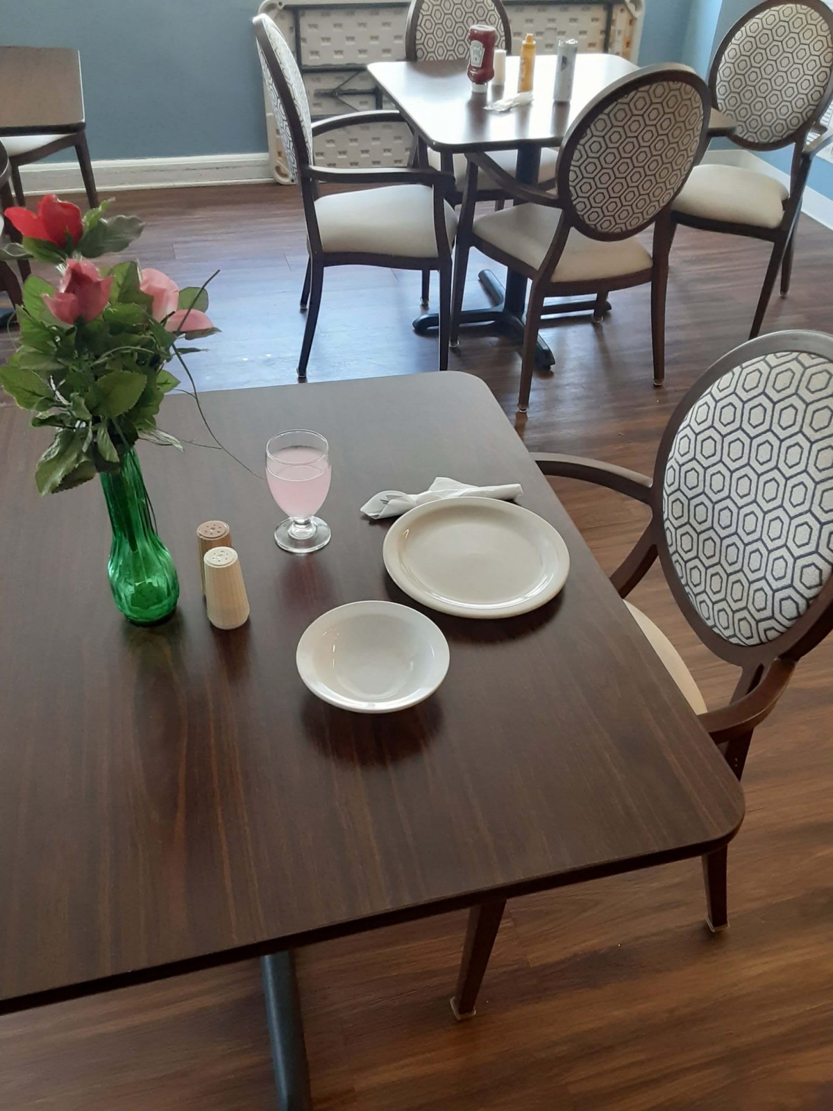 A neatly set dining table with a vase of flowers and a pink drink.