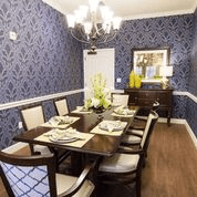 An elegant dining room with a dark wood table, upholstered chairs, and a classic chandelier set against patterned wallpaper.