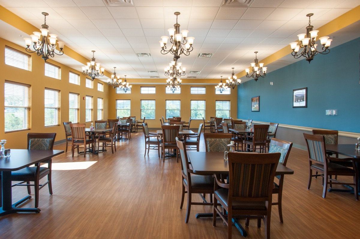 A spacious dining room featuring wooden tables and chairs, large windows, and elegant chandeliers.