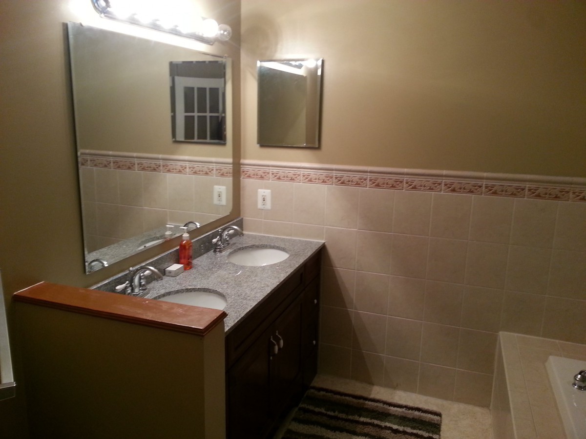 A well-lit bathroom with a large mirror and double sinks on a granite countertop.